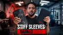  man in a gym holds up two different black neoprene knee sleeves while looking at the camera. The video overlay text reads "STIFF SLEEVES BANNED